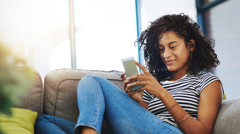 Woman curled up on sofa, scrolling on phone