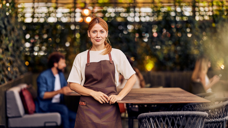 Woman in apron standing in an inviting cafe with a modern and outdoor ambiance.