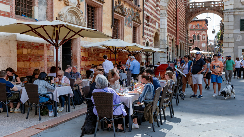 People have lunch on the summer terrace of Caffe Dante restaurant in Piazza dei Signori (with the Loggia del Consiglio and Palazzo degli Scaligeri behind), Verona, Italy