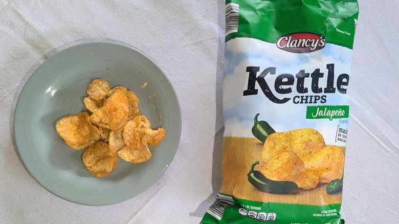 A bag of Clancy's Jalapeño Kettle Chips next to a blue plate of kettle chips
