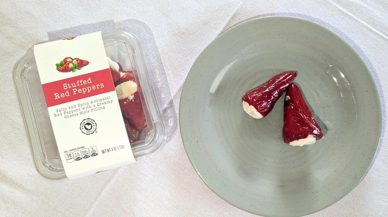 A container of Park Street Deli Stuffed Red Peppers next to a blue plate with two stuffed peppers on it
