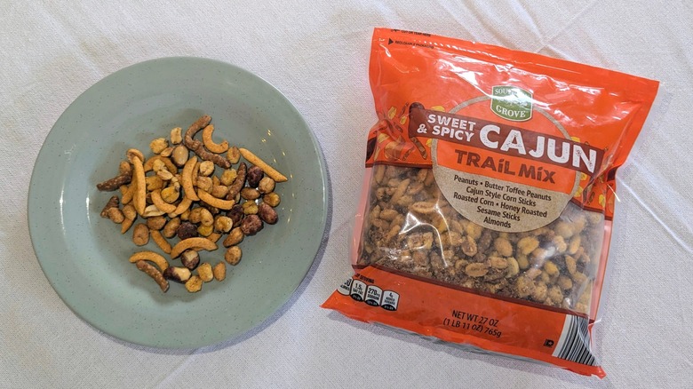 A bag of Southern Grove Sweet and Spicy Cajun Trail Mix next to a blue plate of trail mix