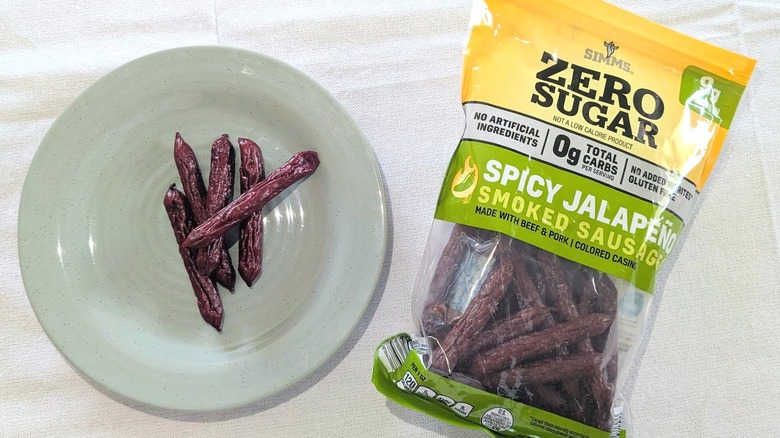 A bag of Simms Spicy Jalapeño Zero-Sugar Smoked Sausages next to sausages on a blue plate
