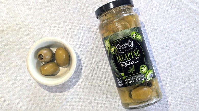 A jar of Specially Selected Jalapeño-Stuffed Olives next to a ramekin of three olives