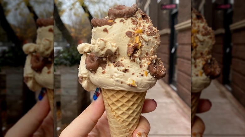A hand holding a cone of malted vanilla gelato with chocolate-covered pretzels.