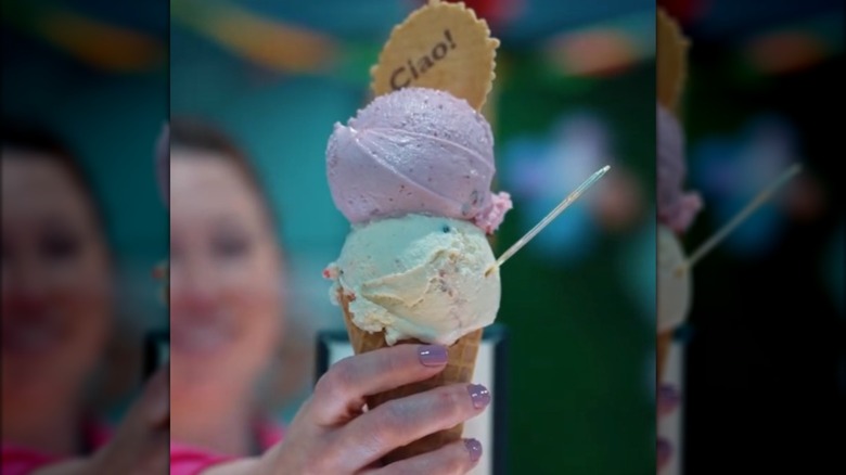 A hand holding two scoops of gelato with a Ciao! cookie in a cone.