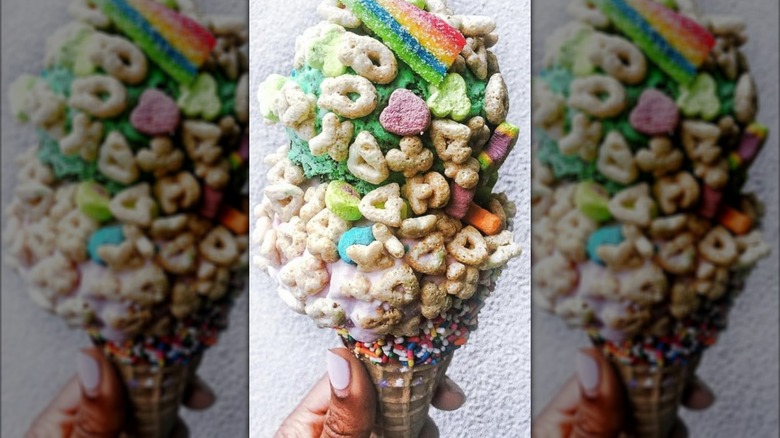 An ice cream cone covered in cereal pieces, sprinkles, and candy.