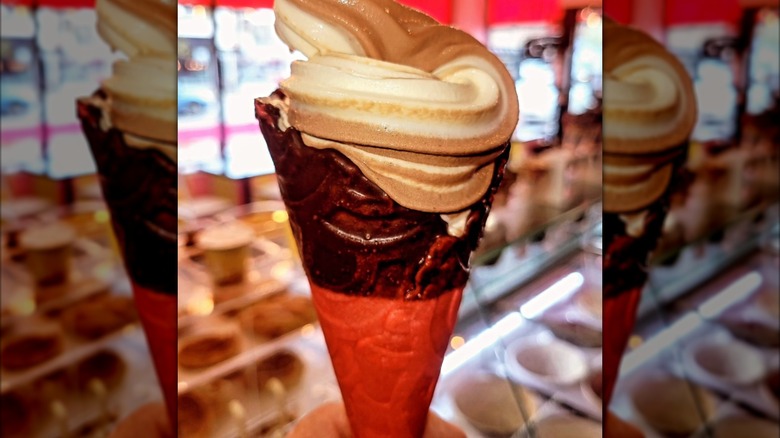 Swirled soft serve ice cream in a chocolate-dipped pink vanilla waffle cone.
