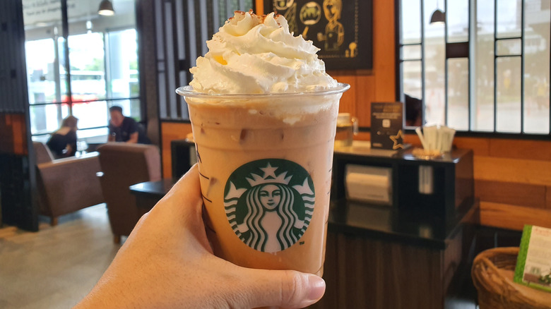 Hand holding iced pumpkin spiced latte from Starbucks