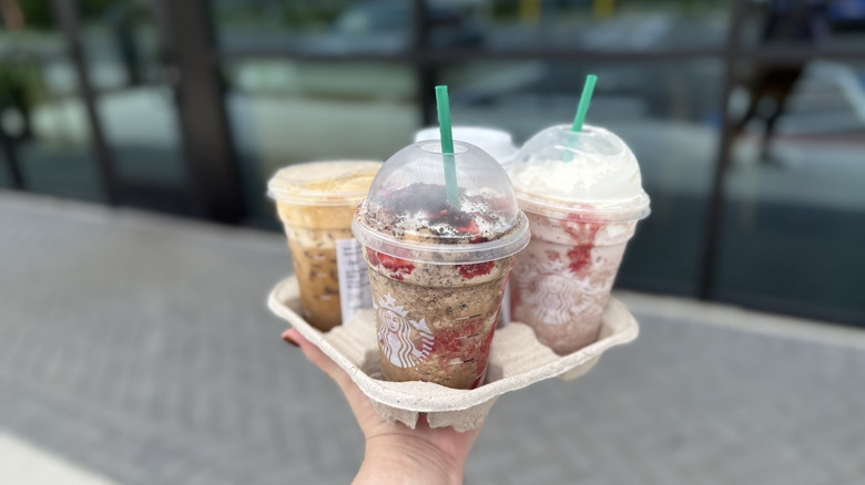 A person holding a to go drink carrier of coffee drinks from Starbucks