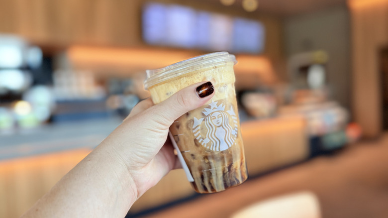 A person holding a Pumpkin Pie Shaken Espresso inside Starbucks cafe