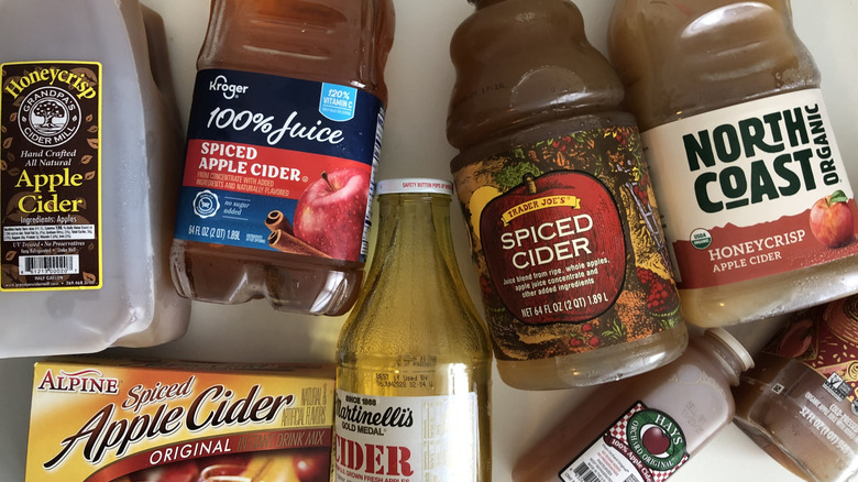 8 Different store-bought apple ciders laid out on desk.