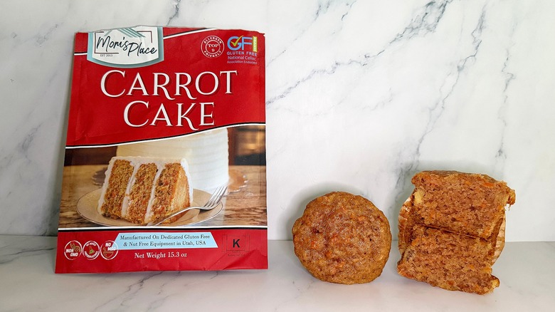 Mom's Place Carrot Cake Mix package next to two carrot cake cupcakes on marble surface