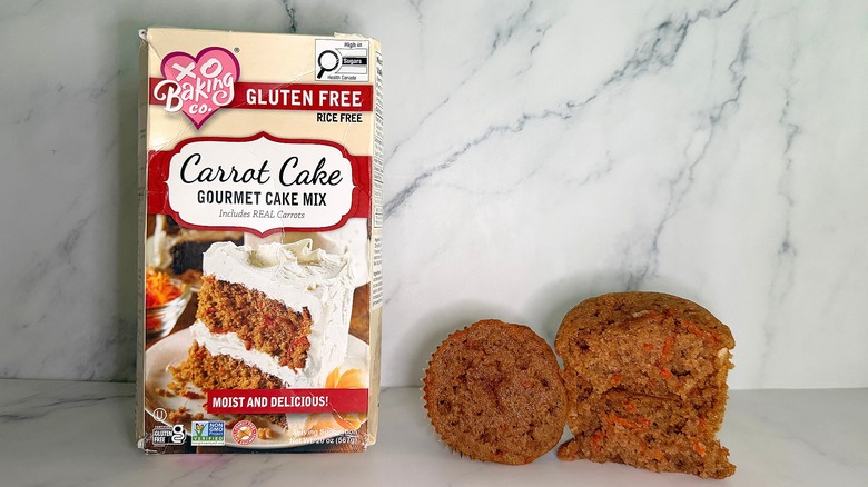 XO Baking Carrot Cake Mix package next to two carrot cake cupcakes on marble surface