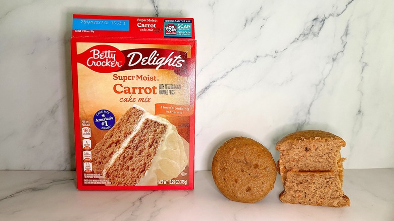Betty Crocker Carrot Cake Mix package next to two carrot cake cupcakes on marble surface