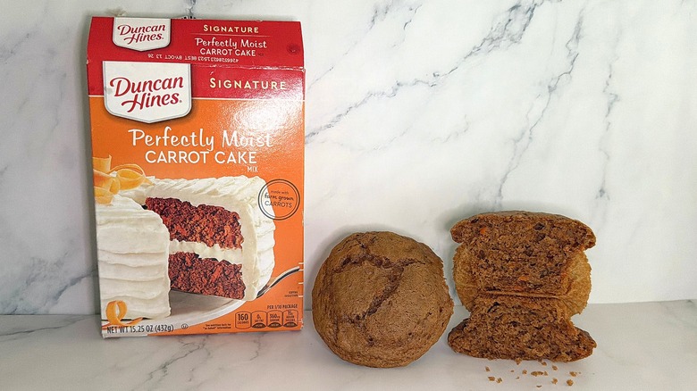 Duncan Hines Carrot Cake Mix package next to two carrot cake cupcakes on marble surface