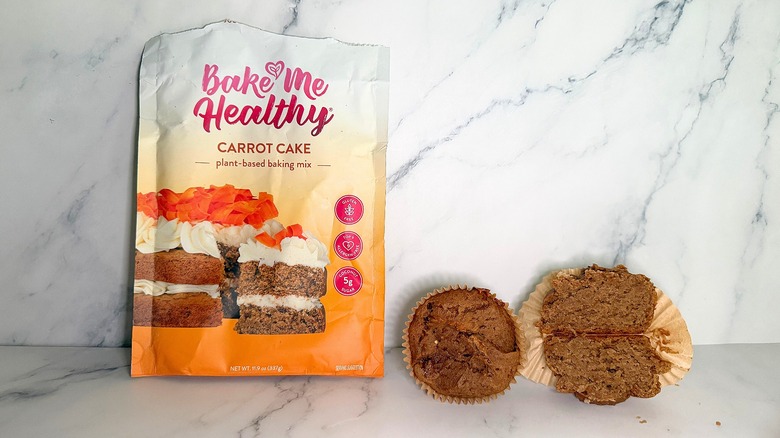 Bake Me Healthy Carrot Cake Mix package next to two carrot cake cupcakes on marble surface