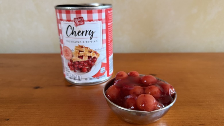 Bowl of cherry pie filling with whole cherries in front of can