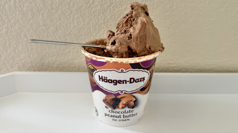 Häagen-Dazs Chocolate Peanut Butter Ice Cream on a spoon with a whole pint on a white table
