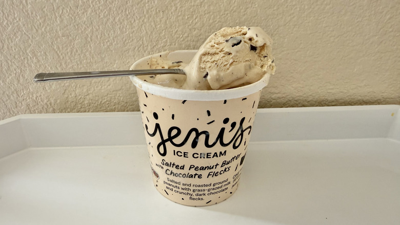Jeni's Salted Peanut Butter with Chocolate Flecks carton on a table with a spoon filled with ice cream placed on top
