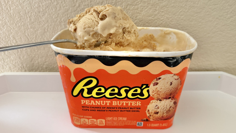 Reese's Peanut Butter Cups ice cream carton on a table with a spoon dug into it