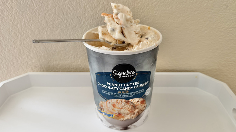 Signature Select Peanut Butter Candy Crunch ice cream in a pint and some of it on a spoon