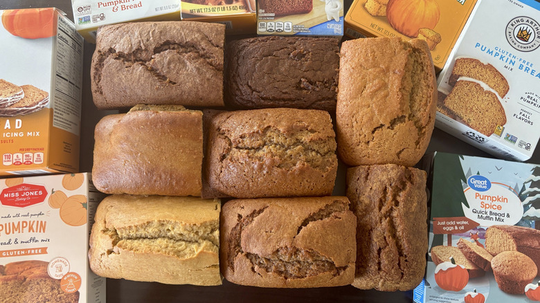 Eight pumpkin breads surrounded by boxes of store-bought pumpkin bread mixes on table