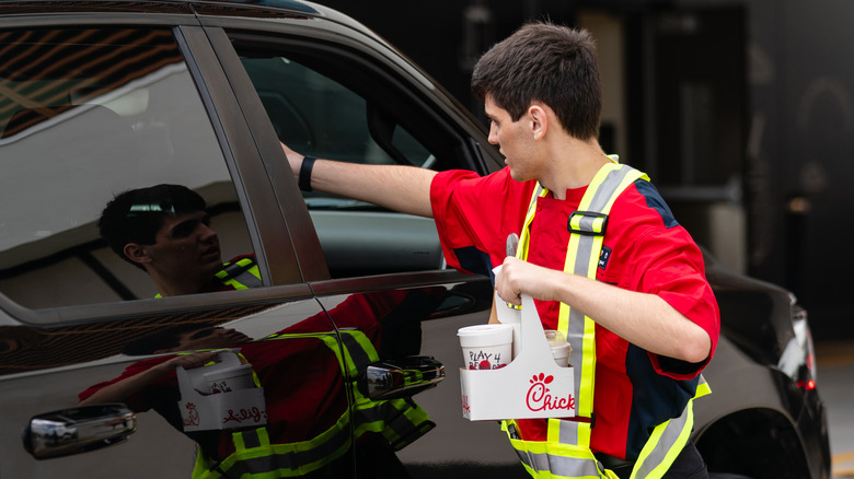 A Chik-Fil-A team member hands an order to a customer in a car