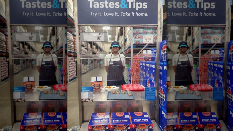 Worker standing under a Tastes and Tips sign and giving out samples
