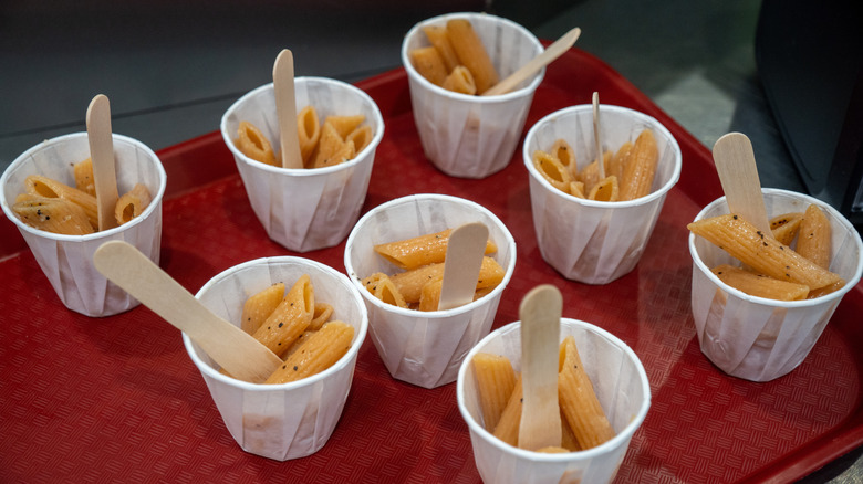 Samples of pasta in paper cups on red plastic tray