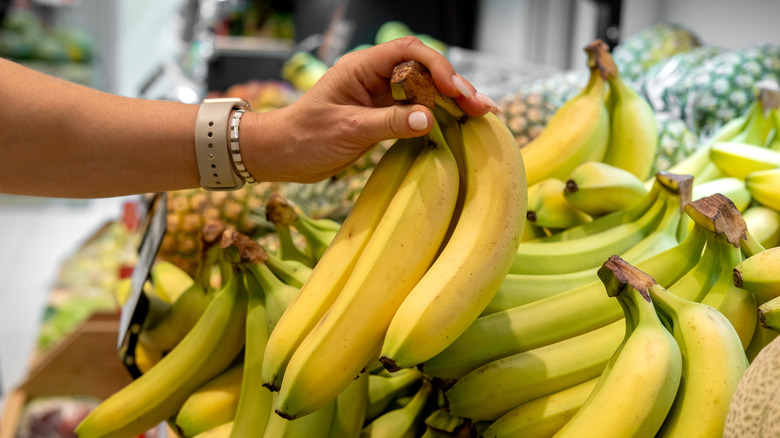 Hand picking up a bunch of bananas from a market stall