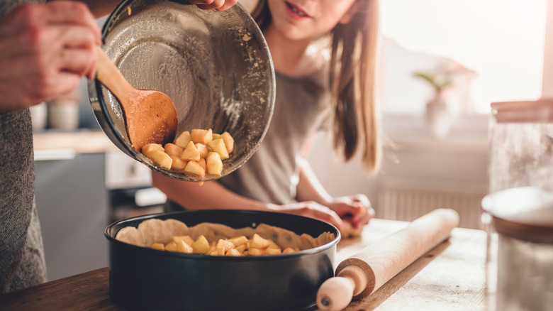Woman pouring chopped apples into a baking pan while her daughter watches