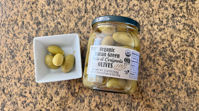 Jar of Organic Italian Green Bella di Cerignola Olives with olives in a white dish