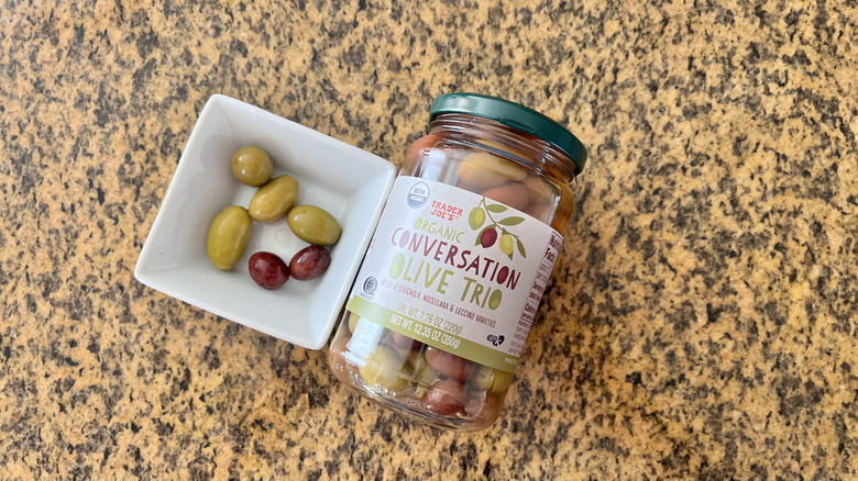 Jar of Extra Large Black Pitted Olives with olives in a white dish