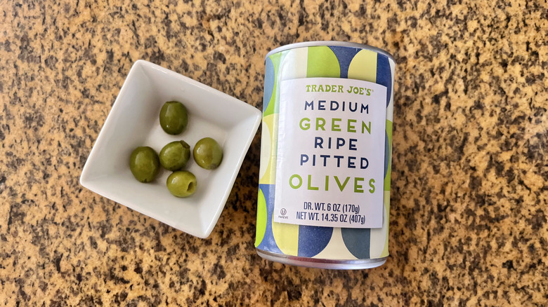 Can of Medium Green Ripe Pitted Olives with olives and a white dish