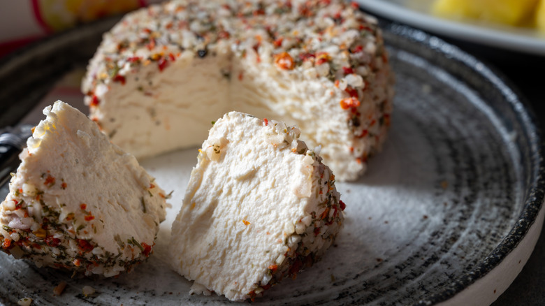 Round goat cheese coated with aromatic herbs on plate with a piece cut off