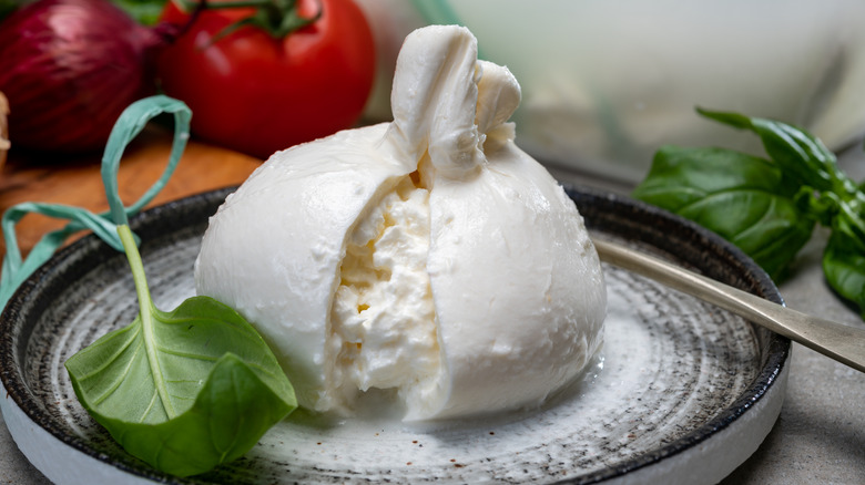 Burrata sliced open to show creamy interior, surrounded by basil, tomato, and onion
