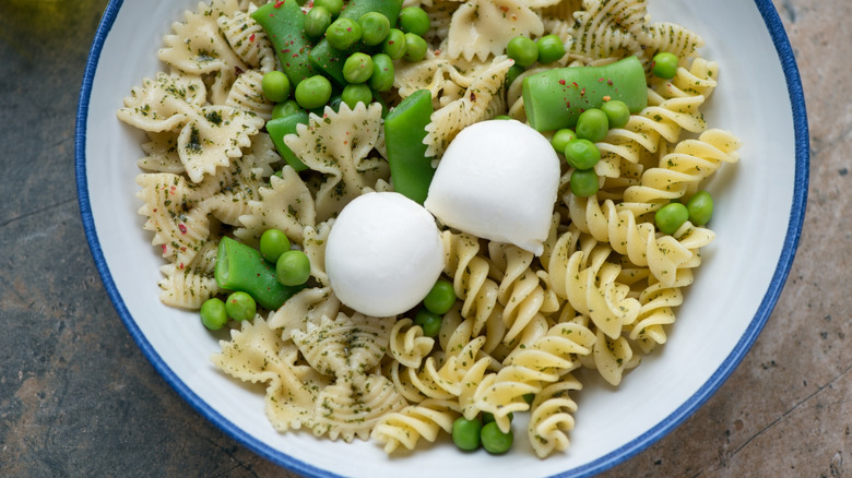 Two bite-sized mozzarella balls on bowl of pasta with peas