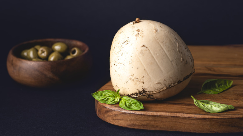 Smoked mozzarella cheese on platter alongside basil leaves and bowl of olives