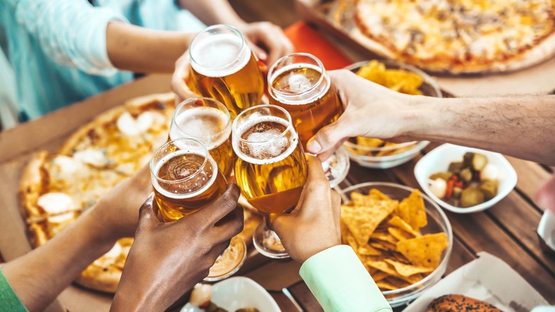 People holding beers and eating pizza