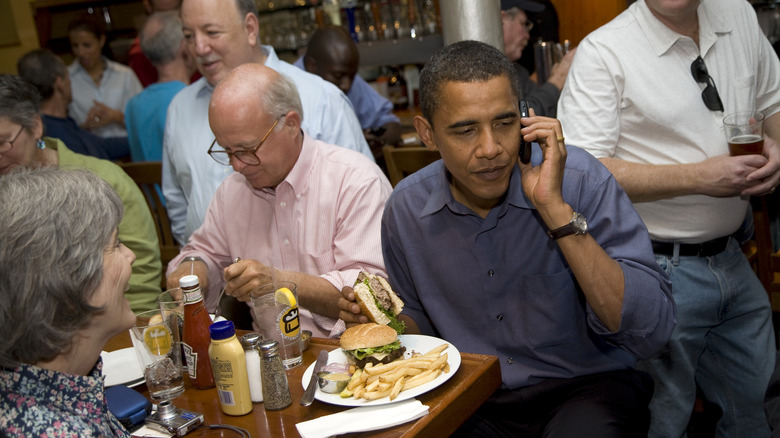 Barack Obama eating a cheeseburger at a crowded restaurant