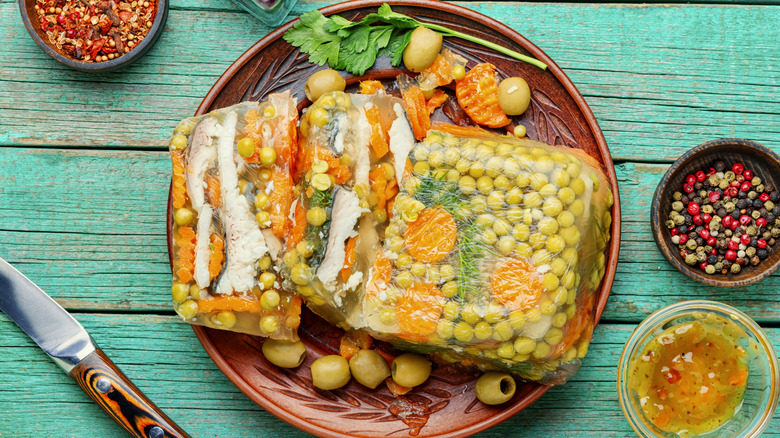 fish in aspic with vegetables, served on a dark terra-cotta plate, against a background of rustic, blue-green wood