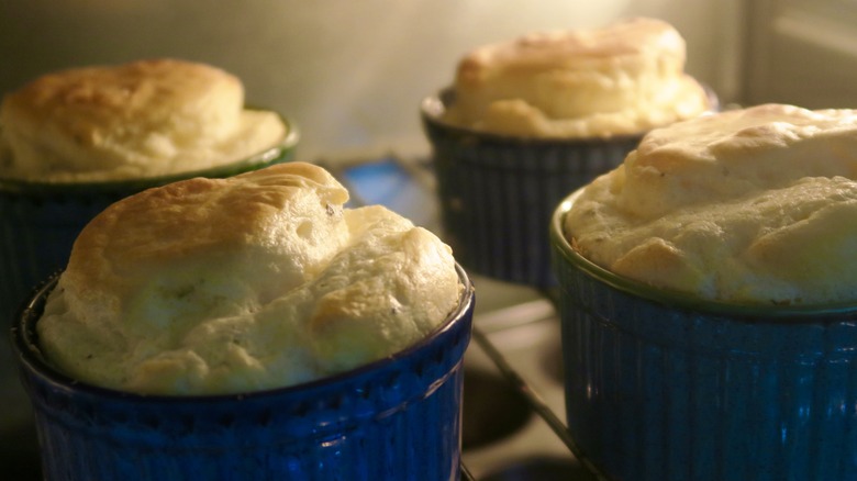 four souffles in small blue ramekins, pictured in the oven as the tops begin to become golden brown