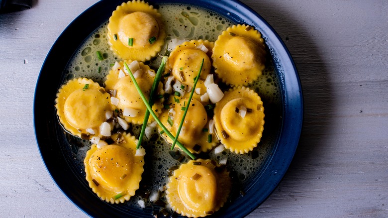 lobster ravioli served restaurant-style with a garnish of chives and a foamed sauce, pictured on a black plate