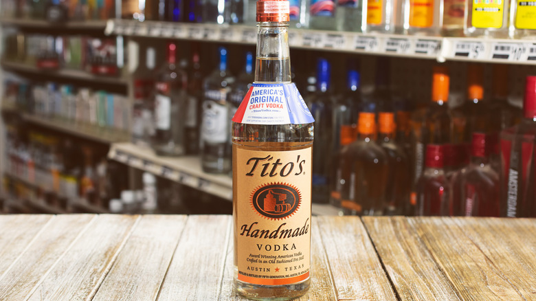 Bottle of Tito's vodka on a wooden board with other bottles behind.