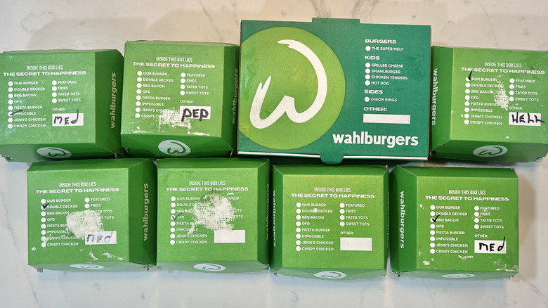 8 different Wahlburgers burgers in green to-go boxes.