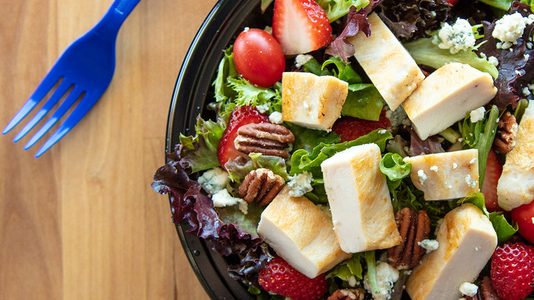 A salad sits on a wooden table next to a blue fork