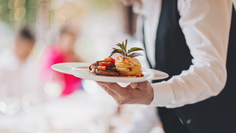 Waiter in uniform carrying elegant plate of food