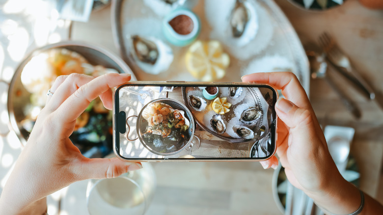 Someone taking a photo of a raw seafood spread with their phone