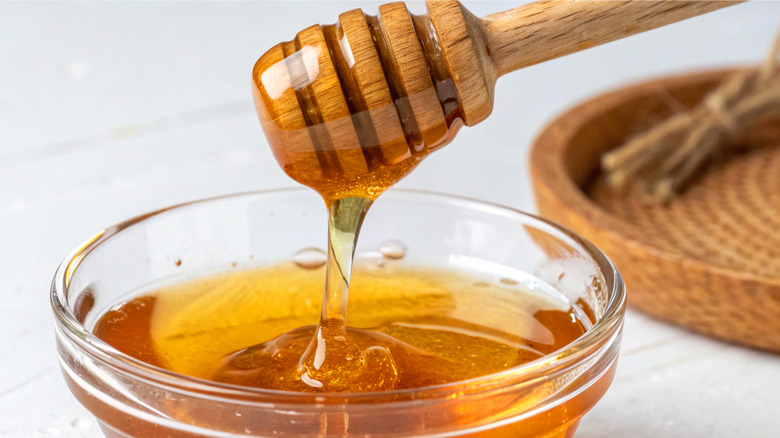 A glass bowl of honey with a wooden honey dipper